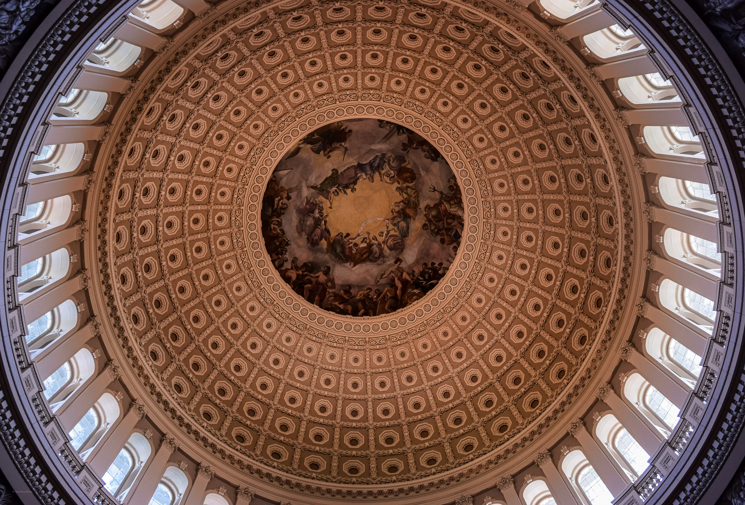 The coffered interior of the United States Capitol dome seen from directly below, ring upon ring of recessed panels narrowing toward the Apotheosis of Washington fresco at the center.